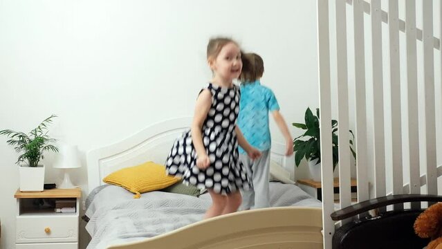 Happy kids are having fun in the bedroom at home. Children jumping on bed. Caucasian boy and girl are cheerful and enjoying their childhood.