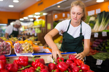Portrait of teenage girl working in supermarket as job experience, selling red pepper