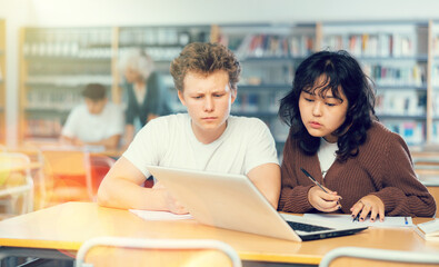 Boy and girl study together at laptop while sitting in a school library