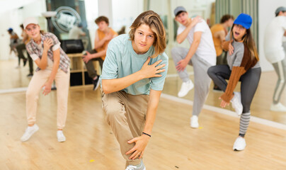 Fototapeta na wymiar Portrait of expressive teenage krump dancer in choreographic studio with dancing teenagers in background. Typical Generation Z .