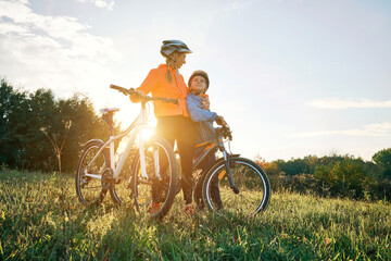 Mother and son ride a bike. Happy cute boy in helmet learn to riding a bike in park on green meadow...