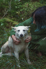 Close up woman embracing white cute mongrel in forest concept photo. Front view photography with woodland on background. High quality picture for wallpaper, travel blog, magazine, article