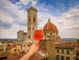 Hand with an Aperol Spritz and a view of the Duomo Cathedral in Florence, Italy