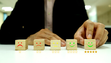 Customer service evaluation and satisfaction survey concepts. The clients hand-picked the happy face smile face icon and five-star symbol on a wooden cube on the table.
