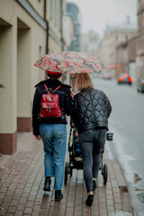Two females walking under one red umbrella and a red backpack in a rainy day in Riga, Latvia