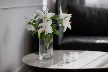 White Lilium Lillie flowers in transparent glass flower cup in beautiful grey interior