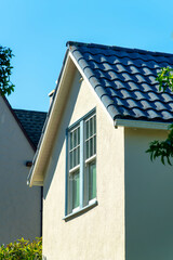 Lone window on side of stucco exterior house or home with dark roof tiles and clear blue sky background