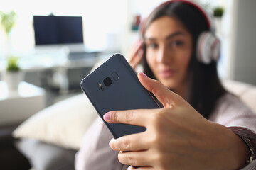 Woman in headphones holds smartphone closeup. Applications for listening to music