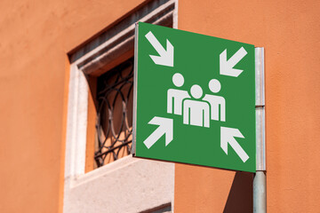Emergency assembly point. Closeup of a green sign in a city against an orange building. Outdoor...