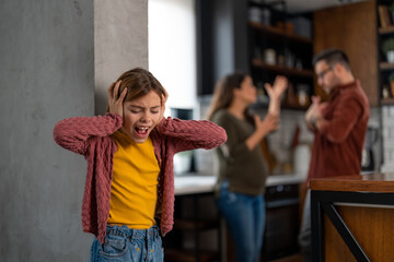 Depressed little girl covering her ears and screaming while her mother and father are having a serious conflict in the background, blaming each other. She can't take it anymore. - obrazy, fototapety, plakaty