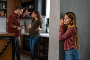 Unhappy child standing from a side, secretly listening to her parents arguing. Frustrated couple...