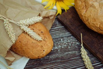 freshly bread with flax seeds, sunflower, ears of wheat on a brown wooden background, home baking