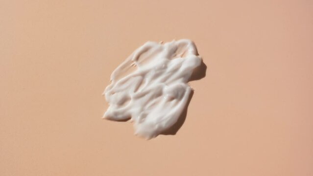 Macro crane shot of white cosmetic lotion smears on beige background | White cosmetic lotion commercial