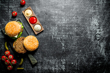 Burgers with French fries, gherkins,tomatoes and different sauces.