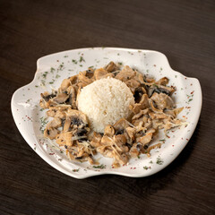 Boiled rice with fried mushrooms and chicken in sauce. Ball of rice in center of plate with mushrooms and chicken around. Serving dish. Dark background. 