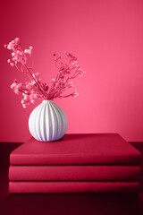 Three books in a purple cover stand on a purple background with a vase of flowers