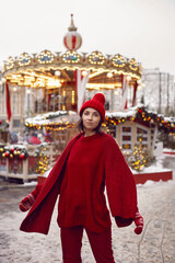 Obraz premium woman in a red warm sweater and hat in winter stands on red square in Moscow against the background of a carousel on Christmas day.