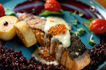 Baked salmon with garnish on a blue plate. Garnish of vegetables, salmon served with sauce and caviar. Soft focus. Close-up. 