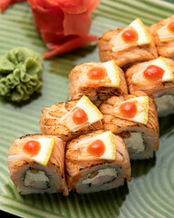 Sushi roll set with salmon, crab and cream cheese, garnished with lemon slices on green plate. Healthy and useful feed. Japanese cuisine. Photo for menu. Top view. Soft focus. Green background. 