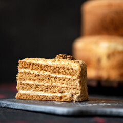Piece of honey cake decorated with walnuts on plank. Cross-sectional view. Eastern European cuisine. Dark background. Close-up. 