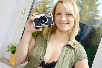 Cheerful woman shoots self-portraits and selfies with old vintage camera at home
