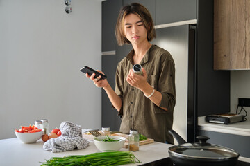 Asian young man checking recipe ingredients on mobile phone.