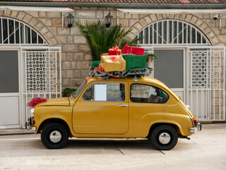 Little yellow vintage car with red, green and yellow gift boxes on its roof side view