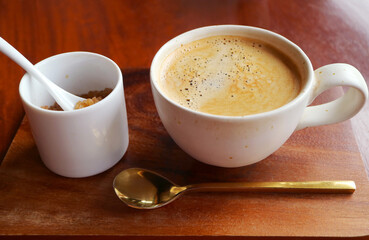 A cup of hot coffee with brown sugar pot and brass teaspoon on wooden table