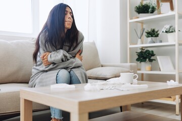 Obraz premium A woman with a cold pills is treated at home chooses which medicines to take and self-medicates, checks the expiration date while sitting at home on the couch, temperature, allergies and covid-19