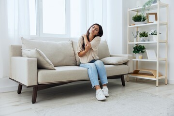 Woman sitting on sofa at home arm and shoulder pain, muscle sprain and joint pain, calcium problems...