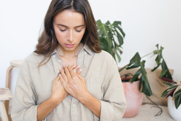 Woman Meditating at Home with Hands on her Heart - obrazy, fototapety, plakaty