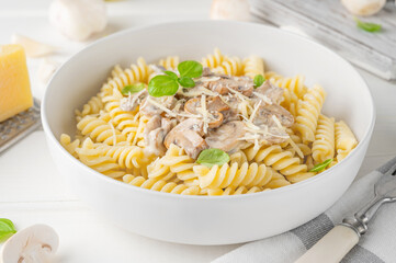 Fusilli pasta with mushrooms, cheese and fresh basil in a plate on a white wooden background.