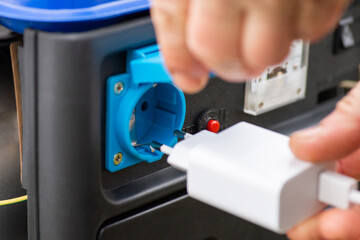 Put on phone charger into the outlet of generator, which produces electricity. Close up of male hand with white plug, concept of charging devices