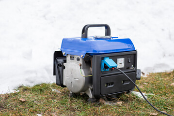 Small generator outdoors while producing electricity. Snow, cold, winter period, blackouts and autonomous supply by electric power