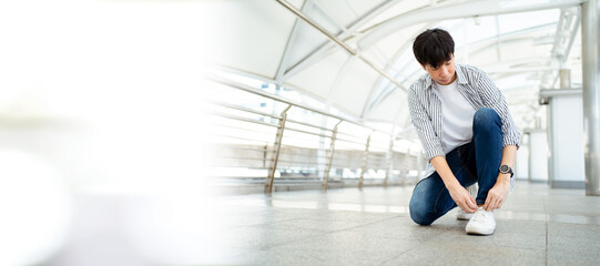 Asian young man sitting on the ground and tie a shoelaces with copyspace. A Man traveling in the city or downtown and tying a shoelace.