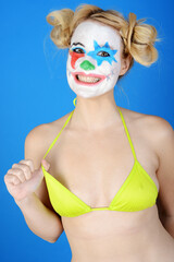 Horror clown in bikini grimaces and poses in front of blue background in studio