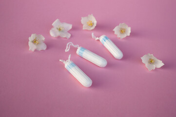 The concept of careful and gentle protection in critical days. Menstruation period concept. Hygienic white tampons for women with flowers jasmine on pink backround.