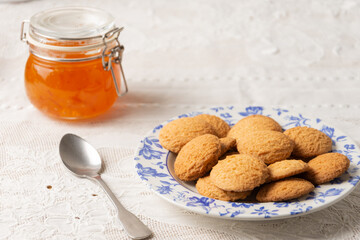 Top view of plate with cookies and jar with peach jam on table with white tablecloth, horizontal, with copy space