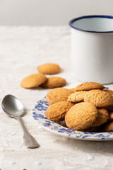 Top view of plate with cookies and white cup with spoon on table with white tablecloth, vertical, white background, with copy space