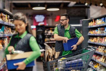 A focused supermarket worker is arranging groceries on shelves at marketplace.