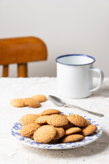 Close-up of plate with cookies and white cup with spoon on table with white tablecloth, selective focus, vertical, white background, with copy space
