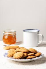 Close-up of plate with cookies, jam jar and spoon on table with white tablecloth, selective focus, vertical, white background, with copy space
