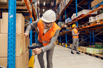 A smiling storage worker is using bar code reader on boxes and goods in storage.