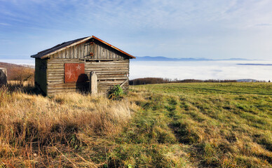 Fototapeta na wymiar Old hut over clouds in pasture mountain landscape.