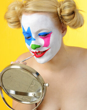 Blonde woman is making up her face as a clown for carnival or halloween	
