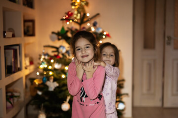Fototapeta na wymiar Two sisters together near Christmas tree at evening home.