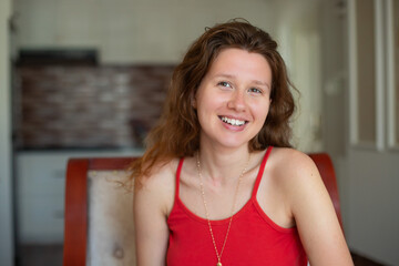 Fototapeta premium Beautiful happy young woman smiling sitting on sofa at home and looking at camera. Portrait of a beautiful girl smiling and relaxing summer 