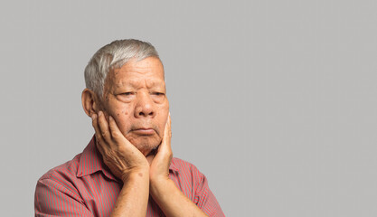 Senior man suffering from a toothache while standing on a gray background
