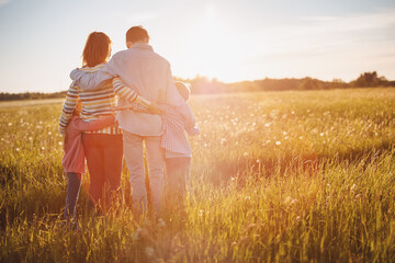 Happy family standing on the summer field and hugging on the sunset with love.