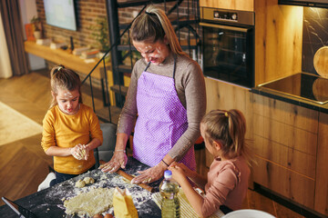 Mother and daughters baking cookies in their kitchen and playing with dough and flour